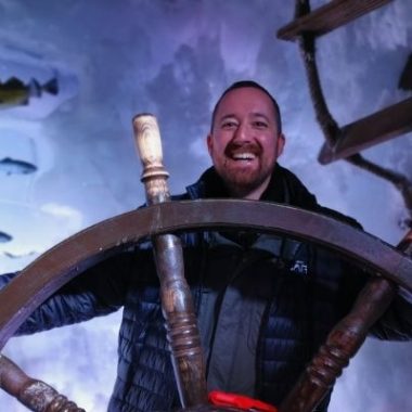 Christian holding a ship's wheel pretending to steer, in front of a sea picture showing fish and water.