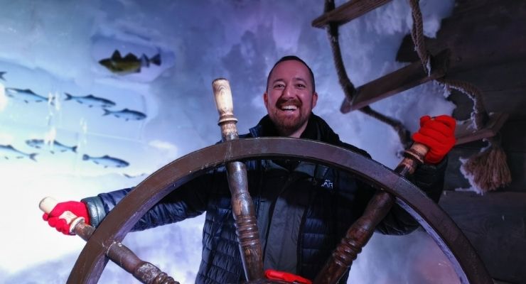Christian holding a ship's wheel pretending to steer, in front of a sea picture showing fish and water.