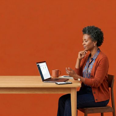 A professional small business owner reviewing digital marketing tools and a website on a laptop at a desk with a vibrant orange backdrop.