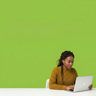Small business owner at a desk looking at a laptop screen, focused expression, plain background.