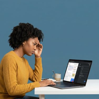Small business owner at a desk looking focused and slightly frustrated at a laptop screen showing website settings.