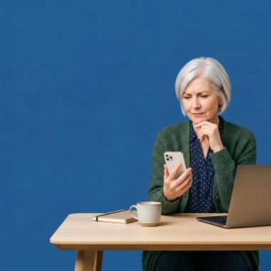 Small business owner looking at a phone with a thoughtful expression, plain white background.