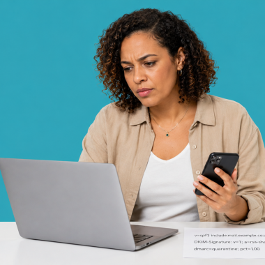 UK small business owner at a laptop checking an email message header, with a printed list of DNS strings on the desk.