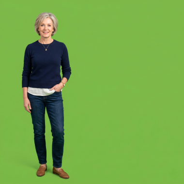 A full-body studio photograph of a smiling middle-aged woman with short grey hair, wearing a navy blue sweater and jeans against a solid lime green background.