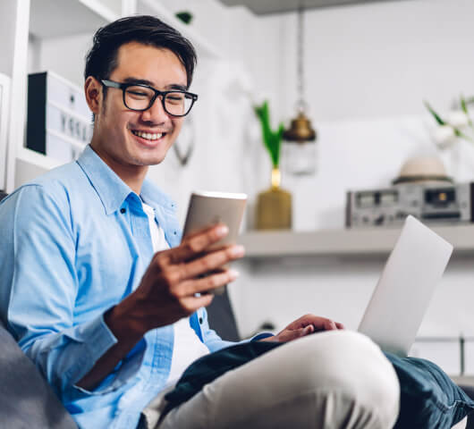 man smiling holding a phone and laptop